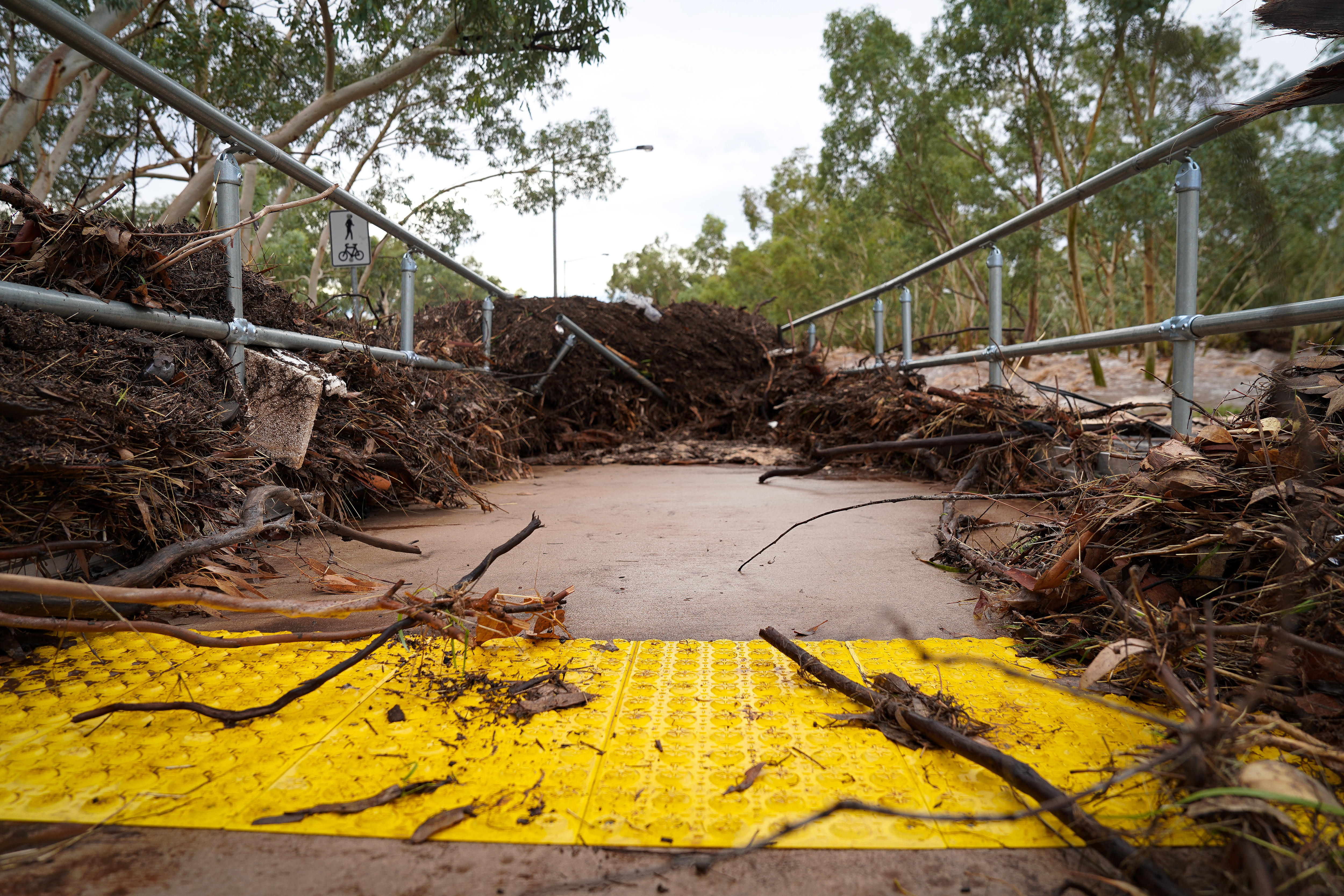 Um caminho coberto de gravetos, folhas e um portão de metal quebrado em uma grande pilha de escombros 
