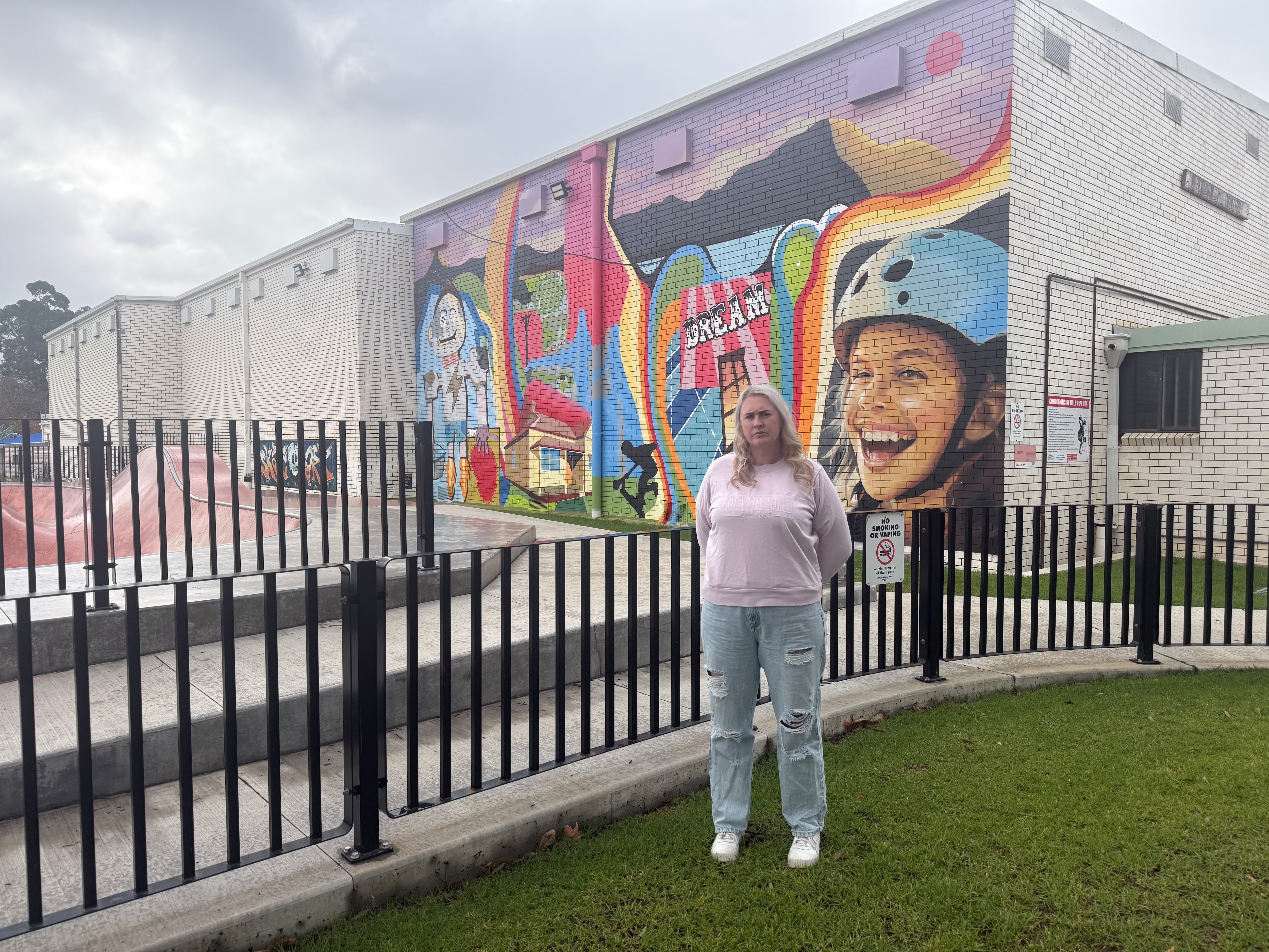 A woman standing next to a fence for a skate park.