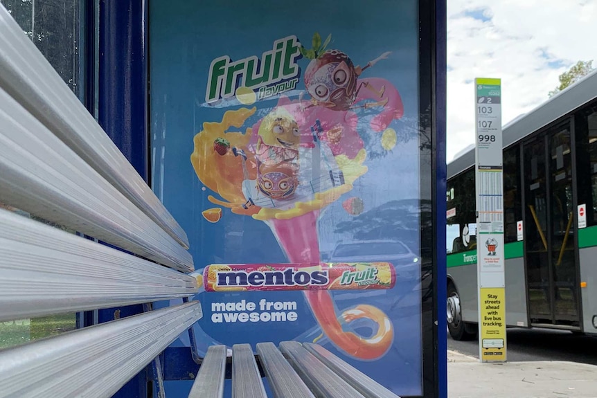An advertisement for Mentos lollies at a bus stop, with a bus off to the right.
