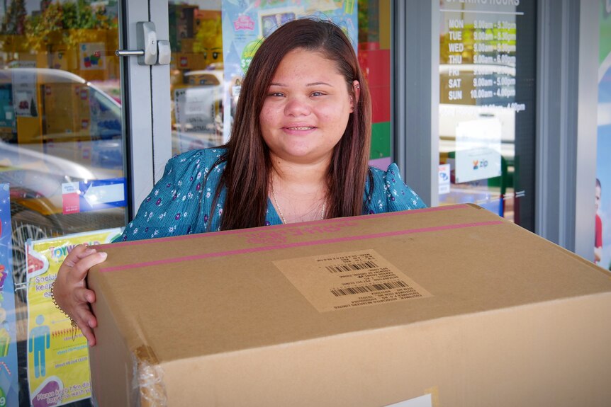 A woman holding a large cardboard box outside a toy shop