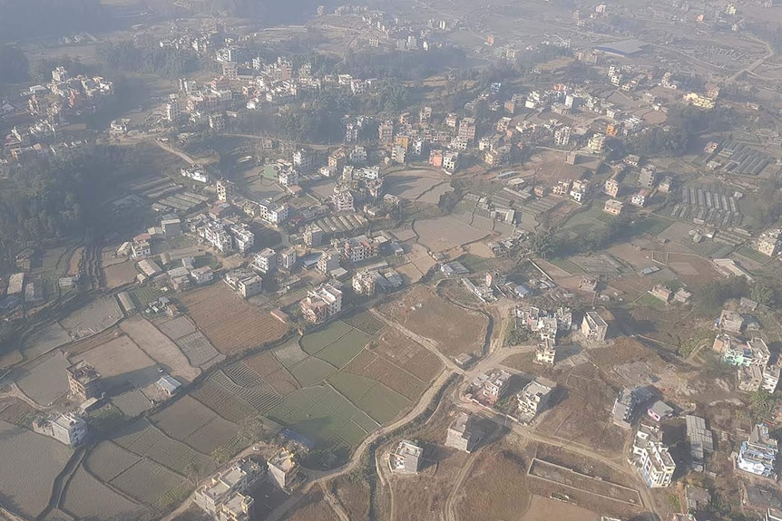 View shrouded through the clouds from a helicopter of villages, buildings and farms in mountainous Nepal.