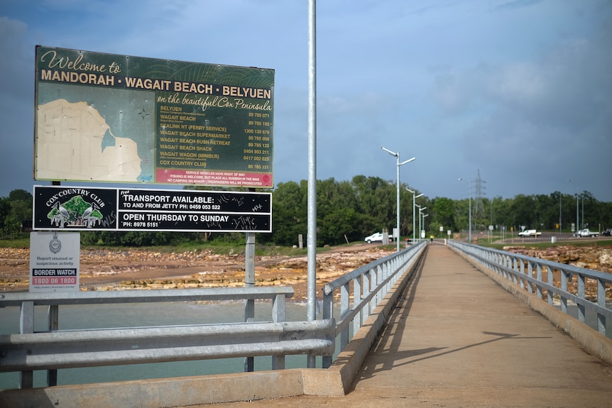An aged sign saying welcome to Mandorah, Wagait Beach, and Belyuen on a jetty.