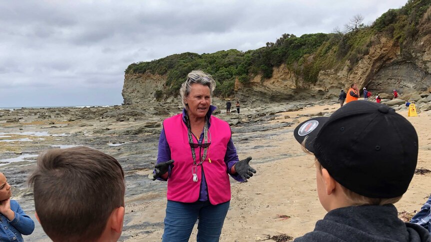 A woman speaks to a family about dinosaurs at a dig site on a Victorian beach