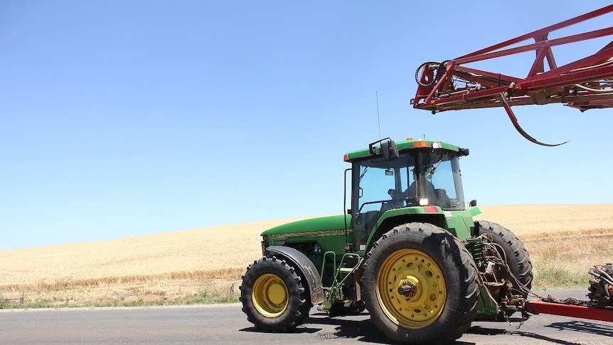 A green tractor driving along the road with a field of wheat in the background.