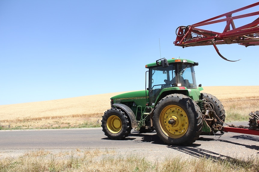 A green tractor driving along the road with a field of wheat in the background.