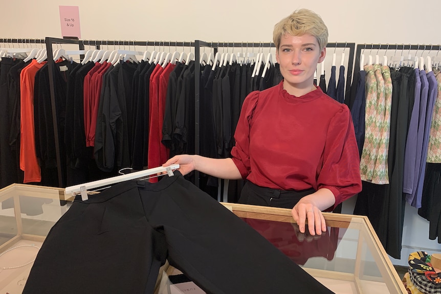 A woman in a red shirt demonstrates a black pants to camera.