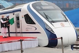 A man holds up a green flag as he stands next to a high-speed train