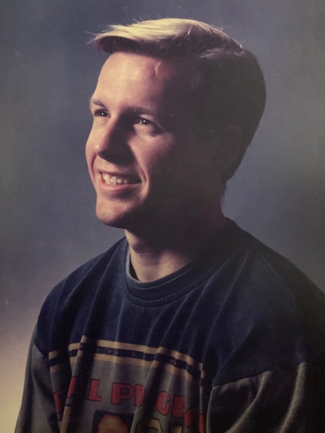 A blonde young man smiles in a portrait.