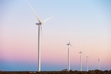 Five giant wind turbines towering over a flat desert landscape at sunset