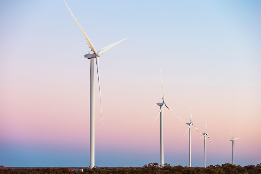 Five giant wind turbines towering over a flat desert landscape at sunset