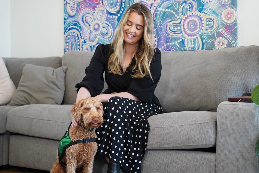 A woman sitting on grey couch with a labradoodle 