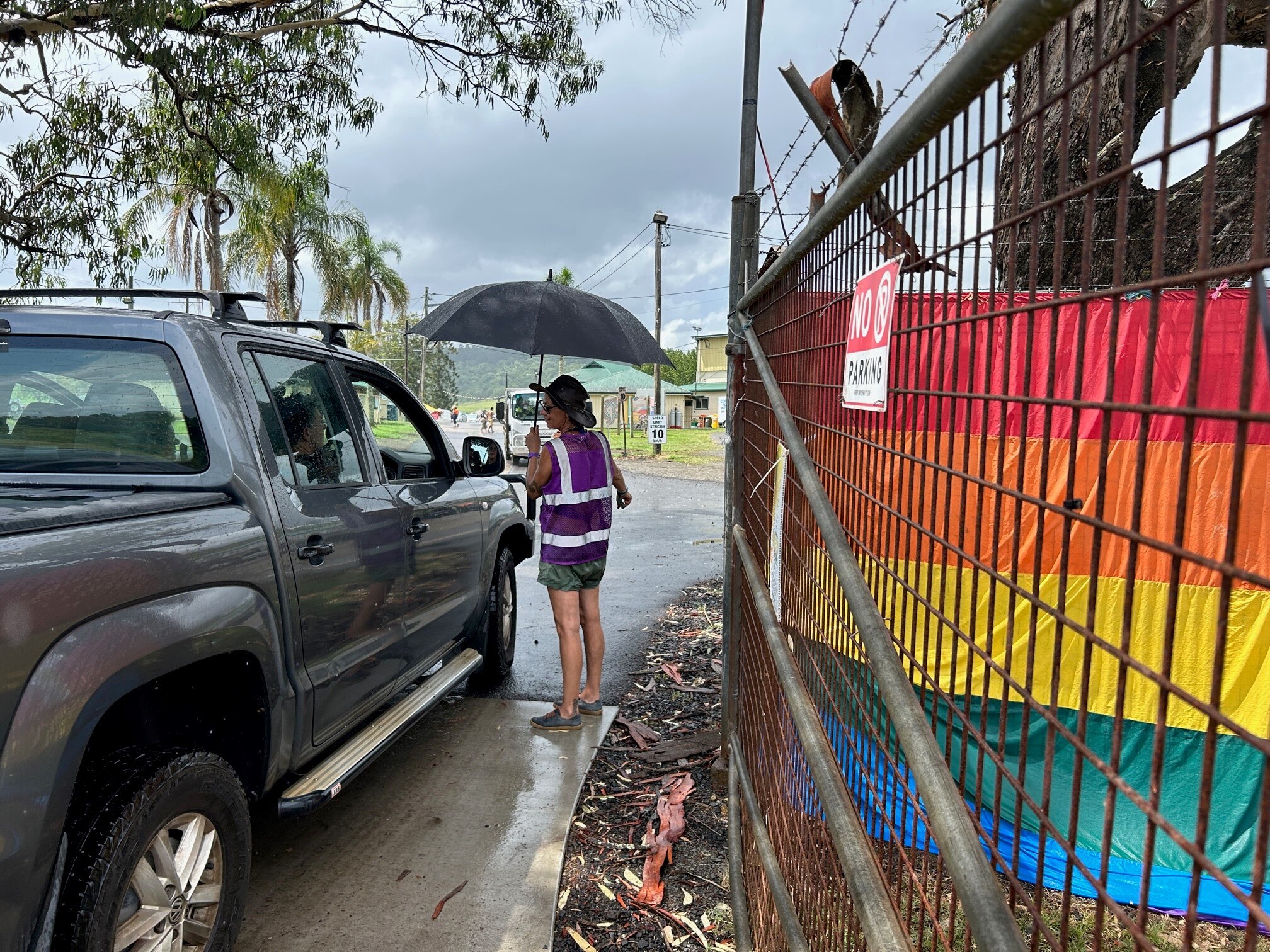 woman with unbrella stands at gate with rainbow flag