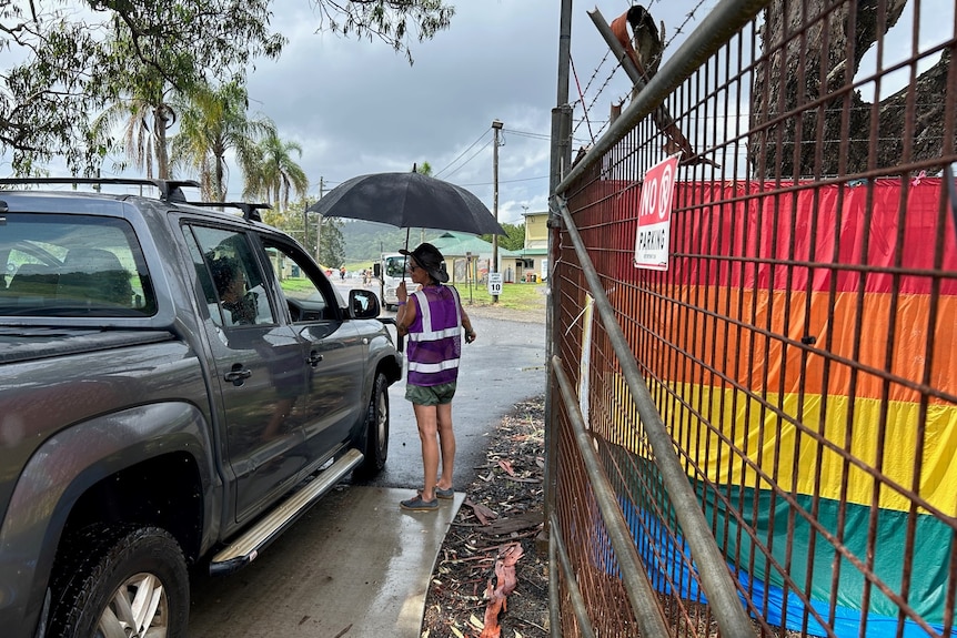 woman with unbrella stands at gate with rainbow flag