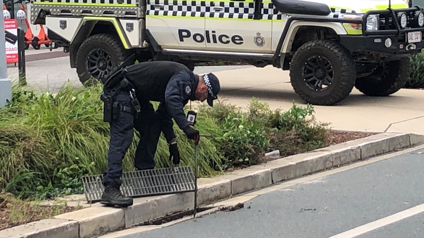 Police officer bending over looking in a drain. 