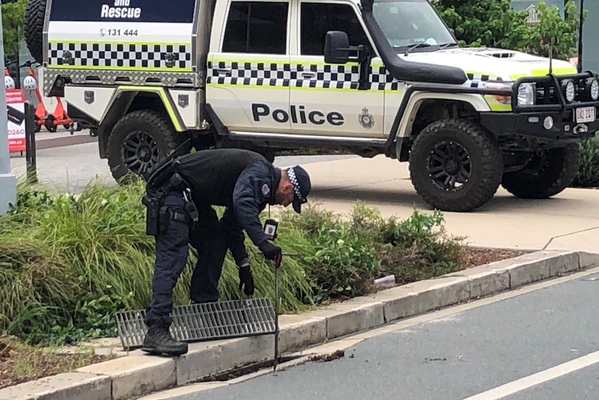 Police officer bending over looking in a drain. 