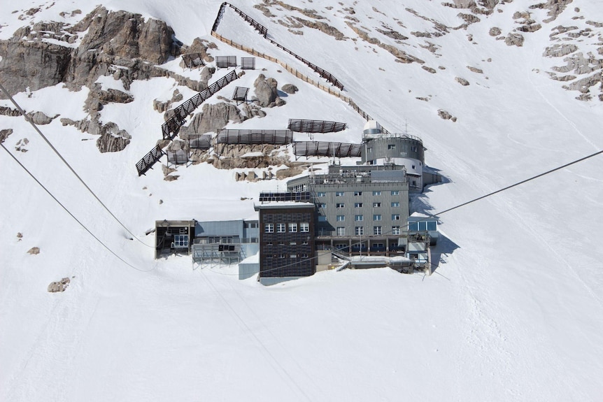 The 12 storey grey building with a round tower and surrounded by snow and stone