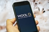 A person's hand holding a smartphone with the WoolQ logo displayed on the screen.