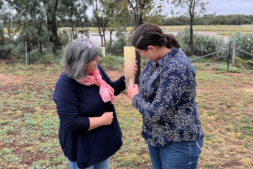 A woman and her daughter stand in a paddock checking a rain gauge.