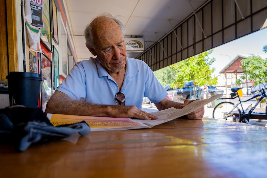A man sits at an outdoor cafe table and reads a newspaper.