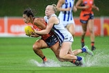 An AFLW player grimaces as she is tackled from behind, as she splashes through a sodden ground.