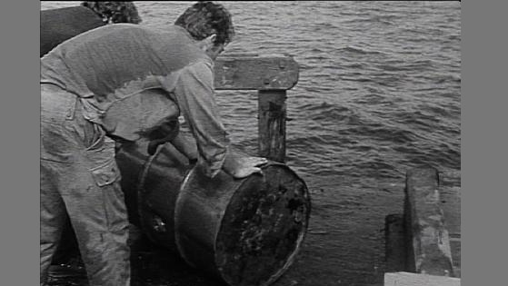 Man stands with oil barrel beside sea