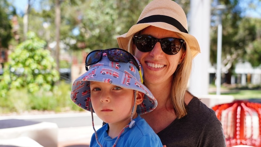 A mum and young son pose for a family photo in an outdoors setting