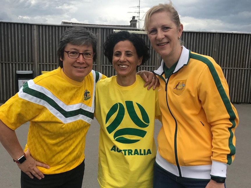 Three women wearing yellow and green outfits pose for a photo together