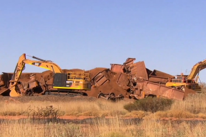 A wide shot showing two yellow cranes in front of the wreckage of an iron ore train.
