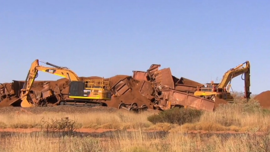 A wide shot showing two yellow cranes in front of the wreckage of an iron ore train.