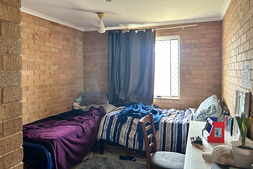 A small room with brick walls has two single beds and a desk inside. 
