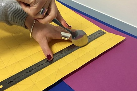 Hand holds a spoon next to a ruler which is laying on a paper with a grid pattern
