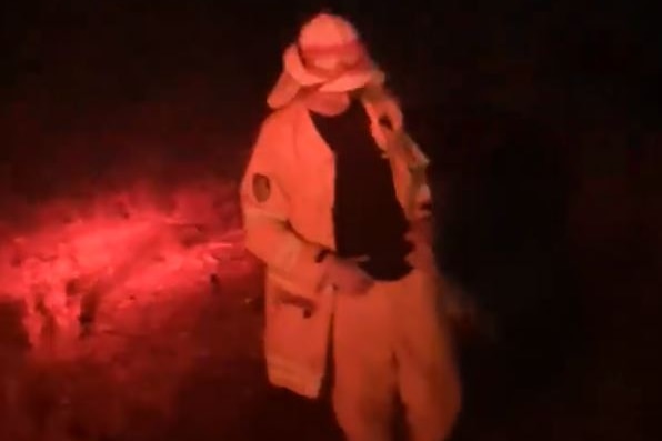 A male firefighter dances in the blue and red lights of a firetruck
