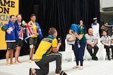 with a backdrop of medal ceremony a man goes down on his knee as a woman holds his face in her hands, bending down in joy