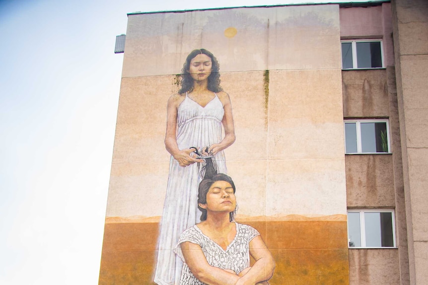 Maria walks past a mural of two women.