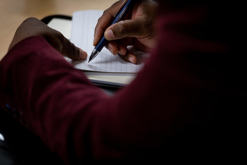 A close up shot of an African man's hands writing on paper with a pen.