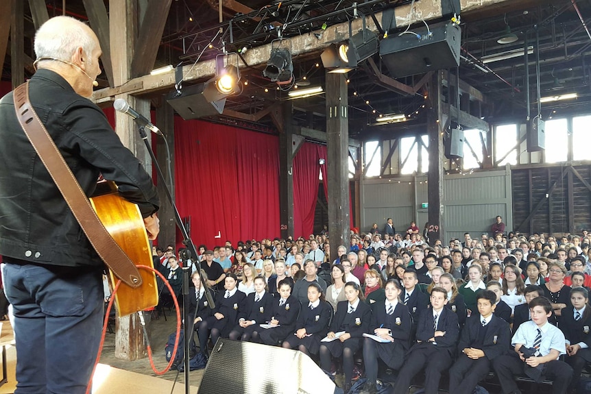 A view from the stage as Paul Kelly performs for a large audience of school students.