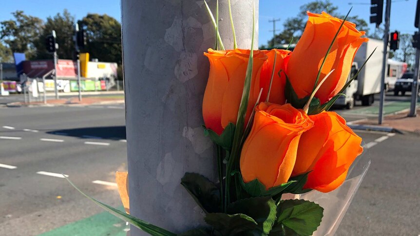 Orange flowers taped to a traffic light pole with a note saying 'RIP'.