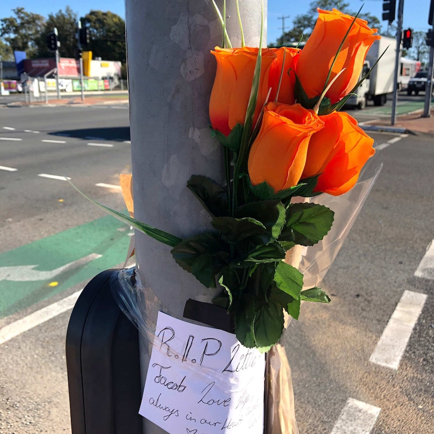 Orange flowers taped to a traffic light pole with a note saying 'RIP'.