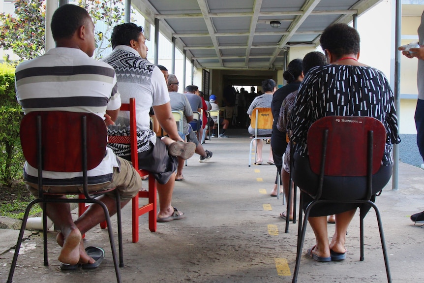 Fijians sit on chairs in an outside corridor waiting to vote