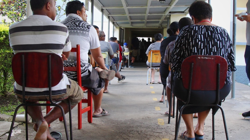 Fijians sit on chairs in an outside corridor waiting to vote
