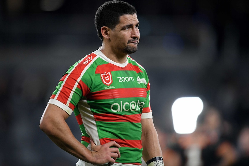 A South Sydney NRL players stands on the field and grimaces during a match.