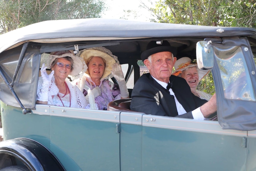 Four people in period costume in an old car