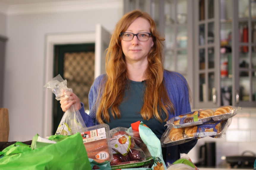 woman holding up produce in plastic packaging in kitchen