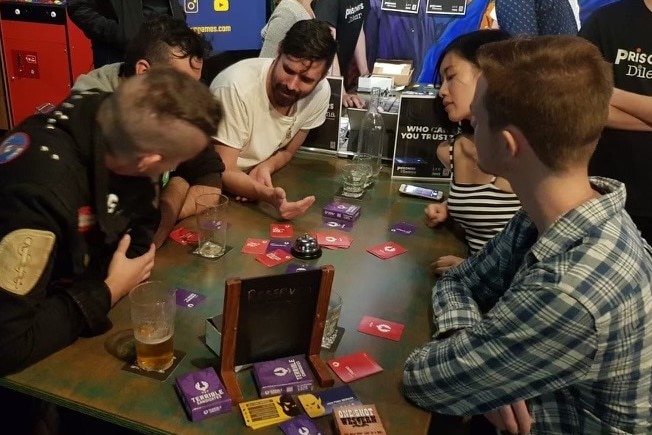Five people sit at a table playing a card game