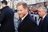 Prince Harry is flanked by two men as he walks along a street