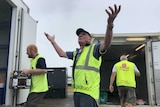 A man in a yellow hi-vis vest throws his hands up in the air as it rains around him