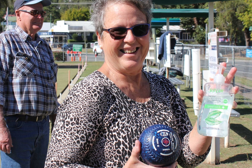 Bowler Wendy Coleman at Canungra Bowls Club holding a bowl and hand sanitiser.