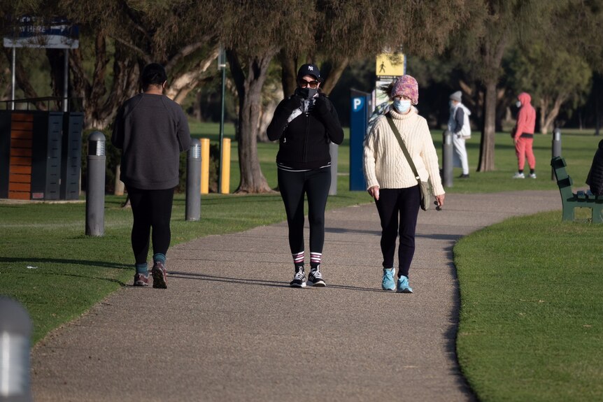 A picture of two women walking towards the camera wearing masks and beanies.