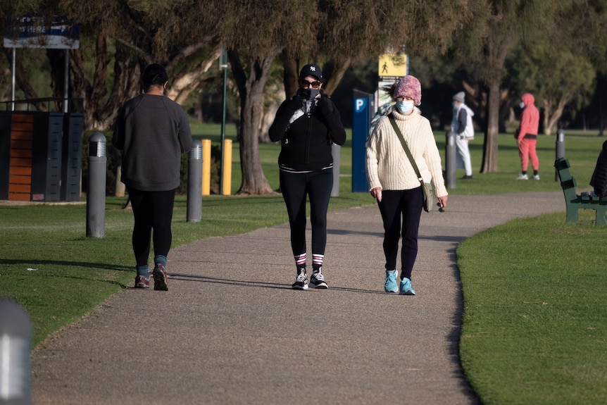 A picture of two women walking towards the camera wearing masks and beanies.