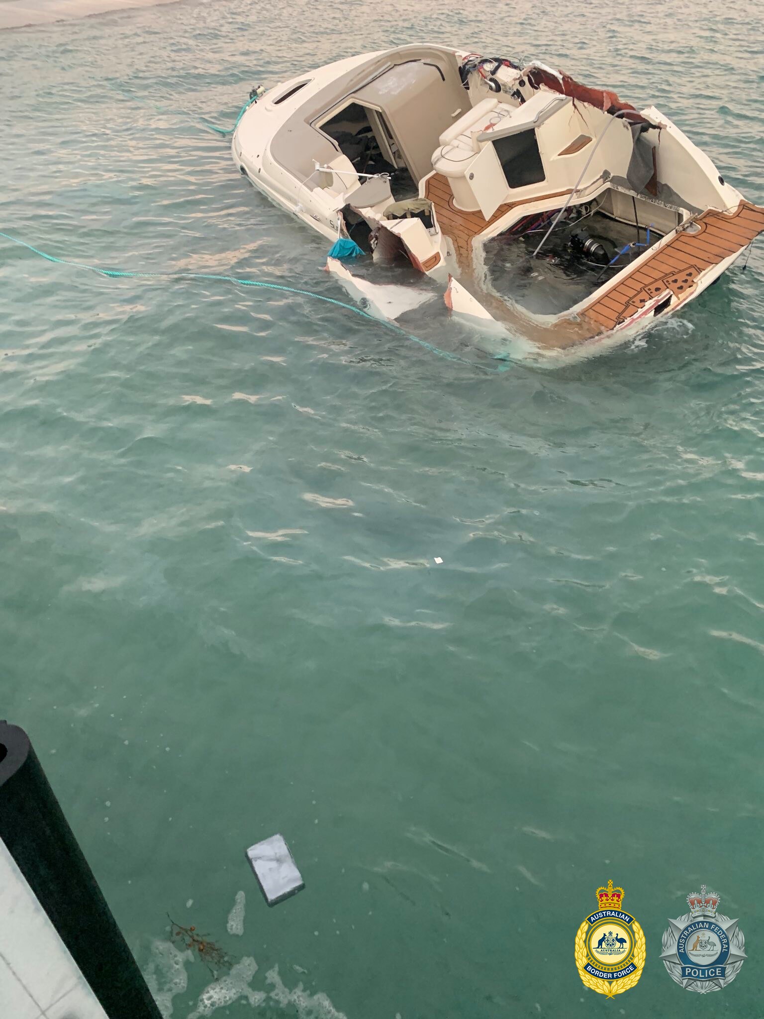 A damaged speed boat in the water. A package of cocaine is in the foreground. 